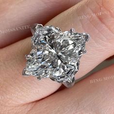 a woman's hand holding a ring with a large diamond in the shape of a flower