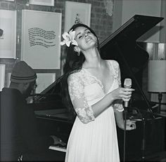 a black and white photo of a woman singing into a microphone in front of a piano