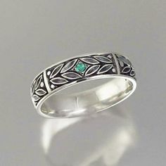 a silver ring with green stones in the center and leaves on it's sides