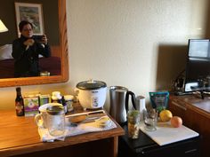 a woman taking a selfie in a hotel room with food and drinks on the counter