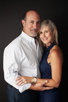 a man and woman are posing for a photo in front of a black background with their arms around each other