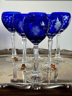 four blue wine glasses sitting on top of a silver tray