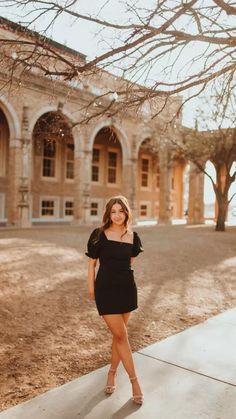 a woman standing on the sidewalk in front of an old brick building wearing a short black dress