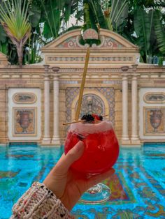 a person holding a drink in front of a pool