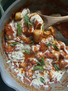 a pan filled with pasta and sauce on top of a table next to a wooden spoon