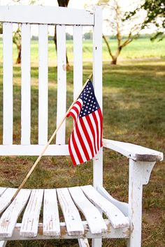 an american flag sitting on top of a white bench in a park with the words happy fourth of july