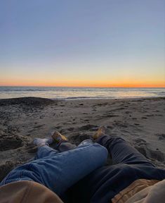 two people are laying on the beach at sunset