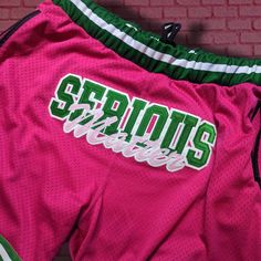 the shorts are pink and green with white lettering on them, along with a brick wall in the background