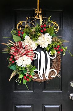 a wreath on the front door is decorated with red and white flowers, greenery, and a monogrammed letter