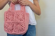 a woman is holding a pink crocheted handbag in front of her face