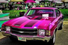 a pink car is parked in front of some tables and chairs with umbrellas behind it