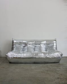 a shiny metal couch sitting on top of a cement floor next to a white wall