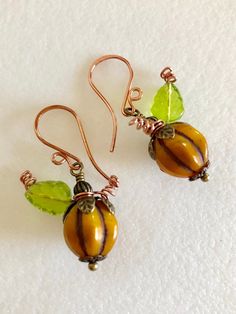 "Darling roasted orange pumpkin Czech glass melon beads wire wrapped with green leaves and copper tendrils on handmade ear wires. Beautiful 12mm opaque Czech glass melon beads in roasted orange squash color with rustic Picasso glaze are wire wrapped with embossed bronze bead caps, Czech olive green glass leaves and copper wire tendrils. Earrings hang from handmade copper ear wires. Total drop is 1 1/2\". Perfect fall accessory!" Artisan Orange Copper Earrings, Handmade Orange Copper Earrings, Orange Copper Wire Wrapped Jewelry, Bead Pumpkin, Paris Charm Bracelet, Diy Earrings Dangle, Pumpkin Idea, Thanksgiving Earrings, Pumpkin Earrings