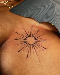 a sun tattoo on the back of a woman's upper body, with small black lines coming out of it