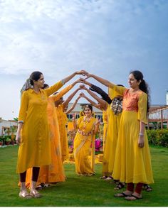 four women in yellow dresses are holding their hands together while standing on the green grass