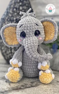 a crocheted elephant sitting on top of a table next to a potted plant