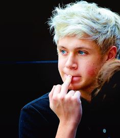 a young man with blonde hair and blue eyes is holding his finger to his mouth