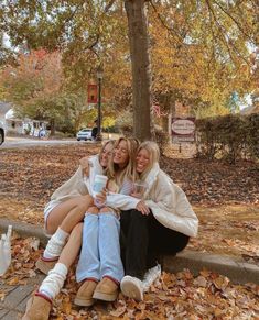 two women sitting on the ground with their arms around each other and holding coffee cups