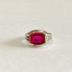 Awesome vintage 10k white gold 1930s era ring featuring a vibrant created ruby! The deep red / pink gem weighs an estimated 3.79 carats, is emerald cut, and securely bezel set. The substantial setting is detailed with decorative designs on the shoulders. Charming vintage piece of fine jewelry for him or her, featuring July's birthstone! ERA - Circa 1930 METAL / MATERIAL - 10k white gold, 1 created ruby (estimated 3.79 carats) [Synthetic ruby contains essentially the same chemical composition &am Vintage Ruby Rings With Polished Finish, Classic Ruby Birthstone Ring, Vintage Red Hallmarked Signet Ring, Classic Red Ruby Signet Ring, Classic Red Birthstone Ring With Center Stone, Antique Red Ruby Birthstone Ring, Classic Red Solitaire Ruby Ring, Classic Emerald-cut Pink Ruby Ring, Vintage Red Birthstone Rings