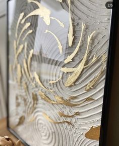 a close up of a framed art piece with gold paint on the glass and wood