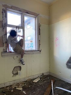 a person sitting on a window sill in a room with torn up walls and debris