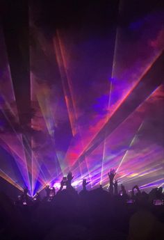 the crowd is at a concert with their hands in the air and lights shining down on them