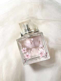 a bottle of perfume sitting on top of a white cloth covered bed sheet with pink flowers