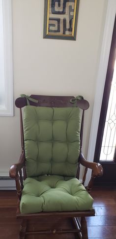 a rocking chair with a green cushion in front of a painting on the wall above it