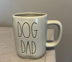 a white coffee mug with the words dog dad on it sitting on a table next to a pillow