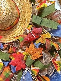 a straw hat sitting on top of a pile of colorful fall leaves next to a ribbon