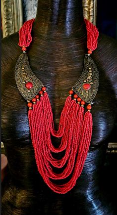 Here's a Bohemian Necklace and Bib Set I found in my inventory. The longer strand is a vintage piece that I did not make. It measures a non-adjustable 28" and closes with a button and a loop. Multiple strands of red-orange seed beads comprise the majority of the piece and two ornate metal accents (looks like bronze) are symmetrically set on each side with an orange-red cabochon (jade??). The shorter necklace is one that I made. It measures a non-adjustable 19" and features the following components: Tibetan resin, Moroccan resin, Zebu bone*, gold tone metal spacers, vintage Chinese brass coins, red branch corals, vintage brass beads and round tiger's eye. Closes with a gold tone hook and eye. Pair them together, or wear separately. These also will mix and match well with your personal favor Adjustable Necklace With Large Beads For Rituals, Adjustable Beaded Necklaces For Rituals, Bohemian Beaded Multi-strand Bib Necklaces, Bohemian Multi-strand Beaded Bib Necklaces, Festival Multi-strand Dangling Beads Jewelry, Festival Multi-strand Jewelry With Dangling Beads, Multi-strand Dangling Beads Festival Jewelry, Beaded Necklaces For Rituals And Festivals, Vintage Red Hand-strung Beaded Necklaces