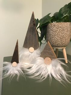 three wooden trees with white feathers are on a table next to a potted plant