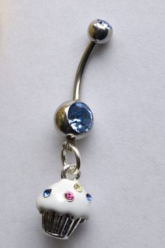 a white cupcake with blue and pink eyes is attached to a silver belly ring