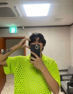 a man taking a selfie in the mirror with his cell phone while wearing a neon green shirt