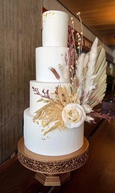 a three tiered wedding cake with feathers and flowers on top is sitting on a wooden table