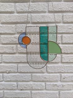 a stained glass sun catcher hanging from a chain on a white brick wall in front of a window