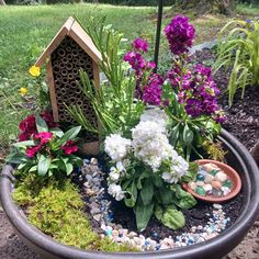 a potted planter filled with lots of flowers next to a bird house and rocks