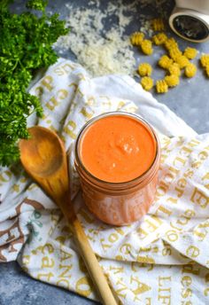 an orange sauce in a glass jar next to some parsley and spoons on a towel