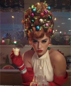 a woman in a red dress with christmas decorations on her head, holding a candle and looking at the camera