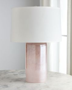 a pink table lamp sitting on top of a white counter next to a large window