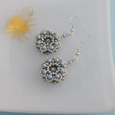 two beaded earrings sitting on top of a white plate next to a yellow flower