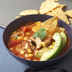 a bowl of soup with tortilla chips and avocado on the side