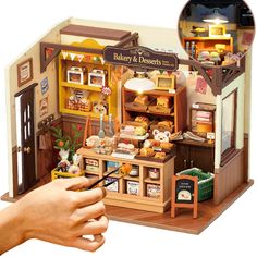 a hand is holding a small model of a bakery and dessert shop with food on display