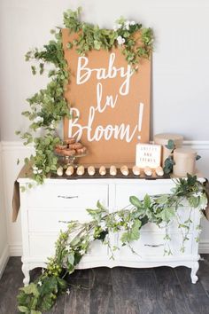 a baby is bloom sign sitting on top of a dresser with greenery around it