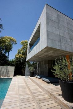 a house that is next to a pool with plants in the foreground and trees on the other side