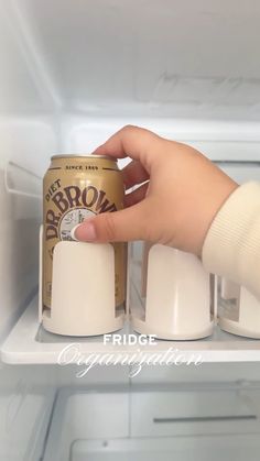 a hand holding a can of brown ale in front of an open refrigerator