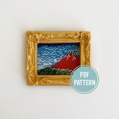 a gold frame with a red mountain needlepoint pattern on it and a blue circle around the edge