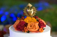 a white cake topped with flowers and a golden heart decoration on it's top