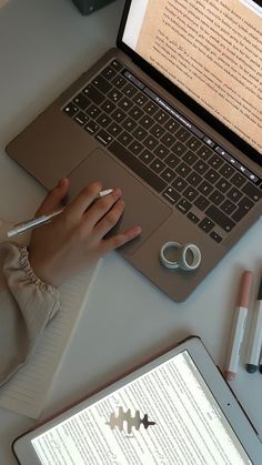 a person using a laptop computer on a desk with writing paper and pens next to it