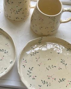 two white dishes with floral designs on them next to a coffee cup and saucer